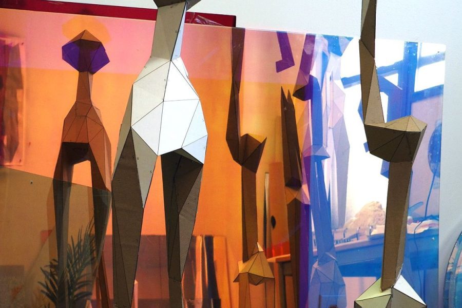 Geometric sculptures made from cardboard are reflected in red, organge, and blue Plexiglas.