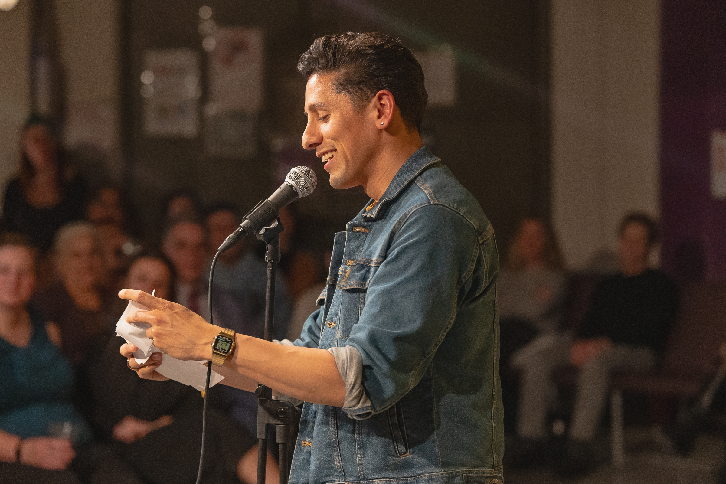 A man smiles and speaks into a microphone.